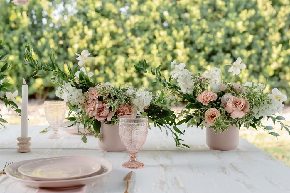 Table setting with floral centerpieces and pink glasses outdoors