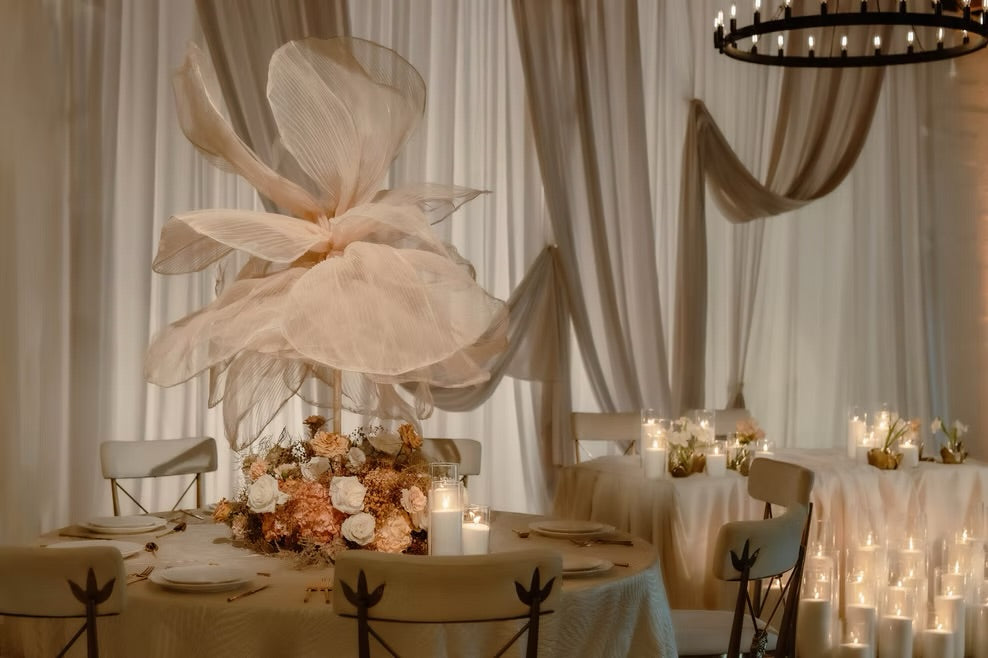 Decorative floral arrangement on a table with candles and draped curtains in the background