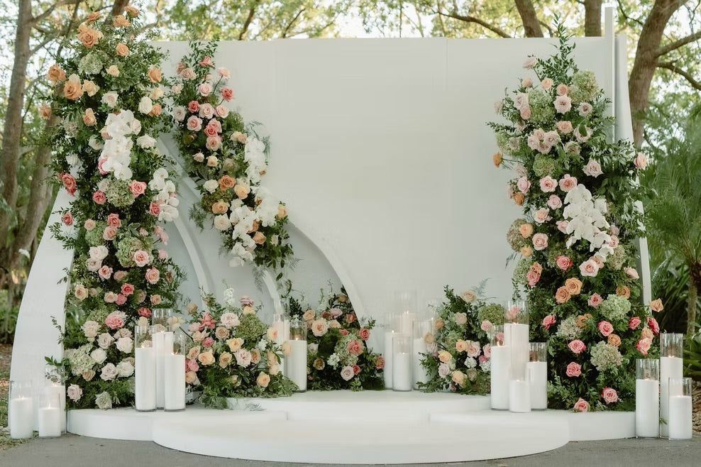 Decorative floral arch with candles against a white backdrop outdoors