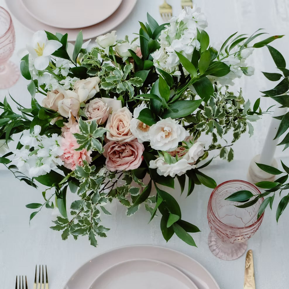Table setting with pink plates, gold cutlery, and a floral centerpiece on a light background