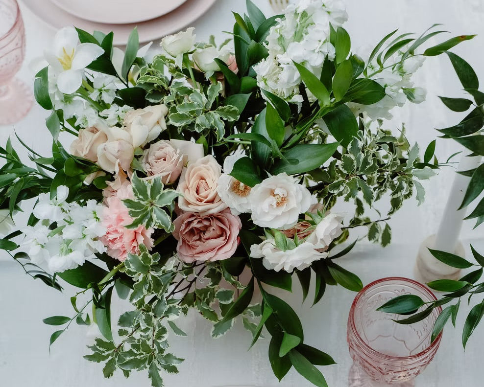 Table setting with pink plates, gold cutlery, and a floral centerpiece on a light background