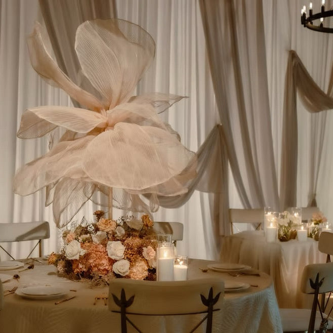 Decorative floral arrangement on a table with candles and white tablecloth in a room with curtains.