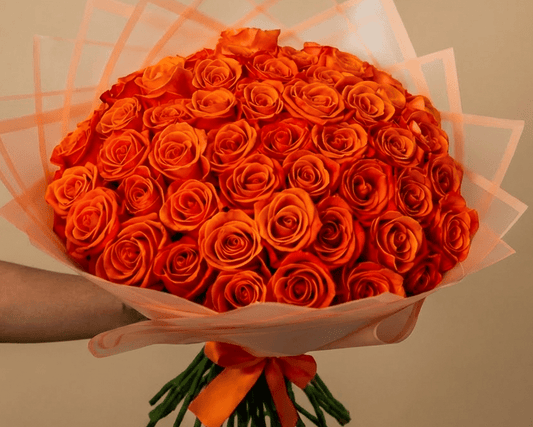 A large bouquet of vibrant orange roses wrapped in pale pink tissue paper and tied with an orange ribbon.