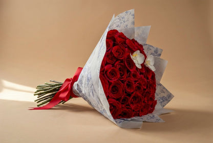 A bouquet of 50 red roses wrapped in white patterned paper with a red ribbon, set against a solid beige background.