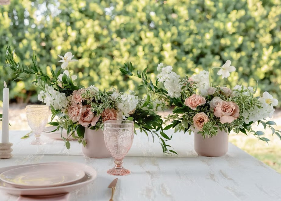 Outdoor wedding reception table with blush and white floral centerpieces, greenery, and pink glassware in Miami