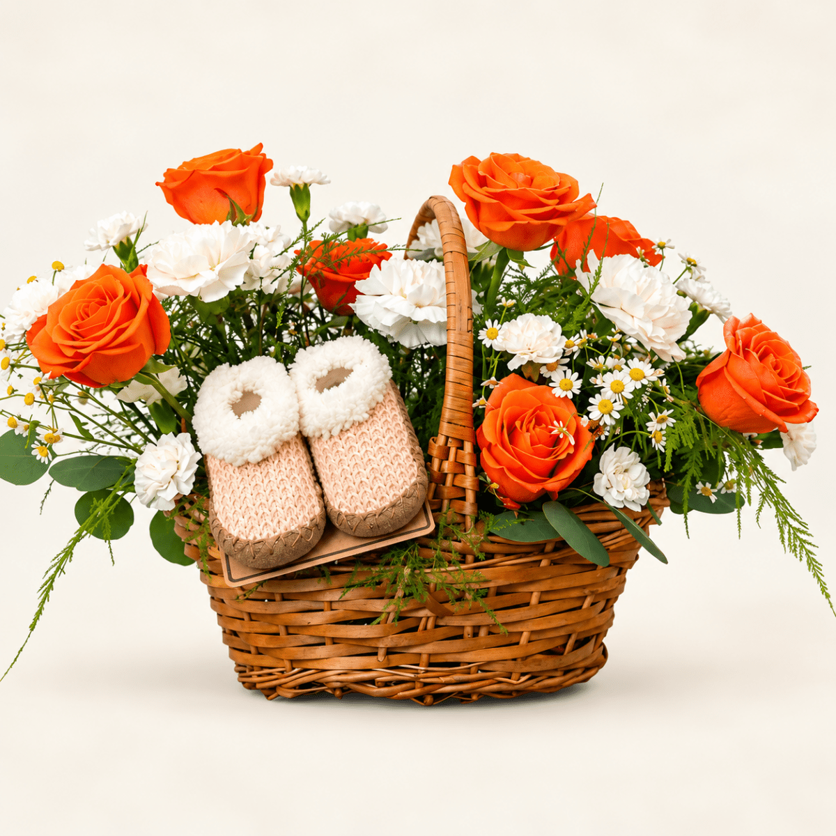 The Little Bloom baby flower basket with orange roses, white flowers, greenery, and baby booties