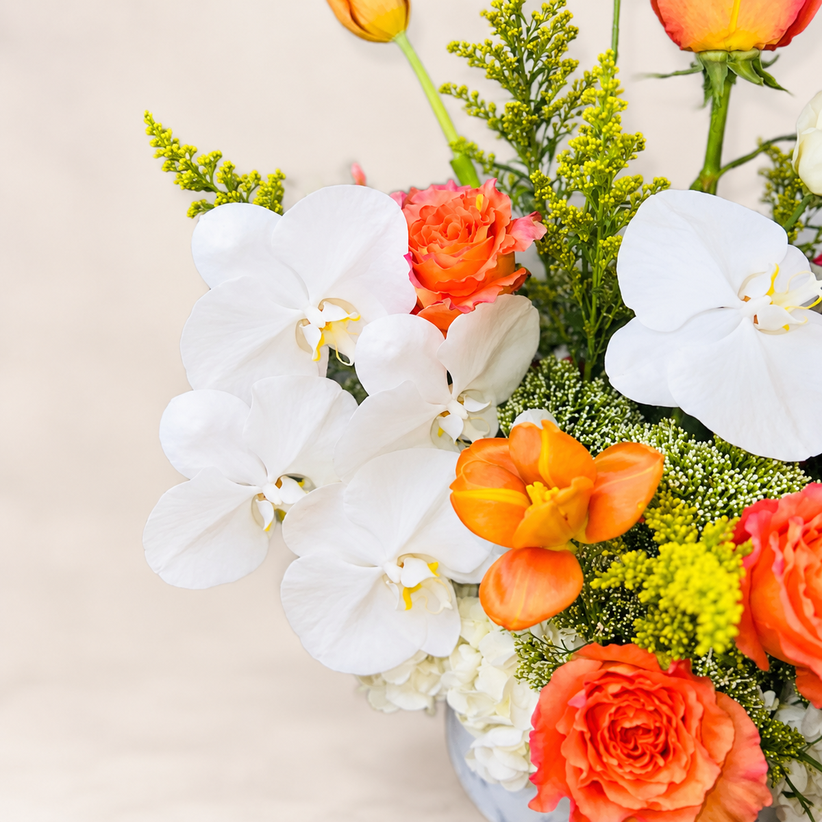 Close-up detail of The Valencia floral arrangement featuring white orchids, coral-orange roses and seasonal flowers