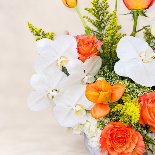 Close-up detail of The Valencia floral arrangement featuring white orchids, coral-orange roses and seasonal flowers