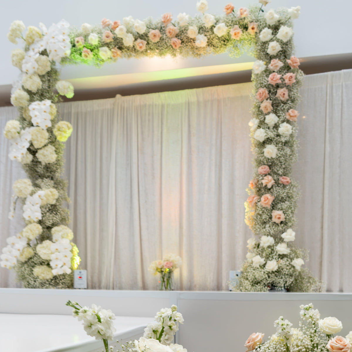 Floral arch and arrangements with white, pink, and green flowers against a neutral background.